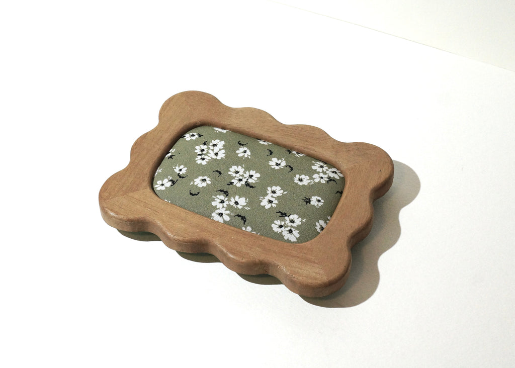 Handmade rectangular Lou The Label jewelry tray with a natural wood frame featuring soft, wavy edges and a sage green floral fabric lining with small white flowers photographed on a white background.