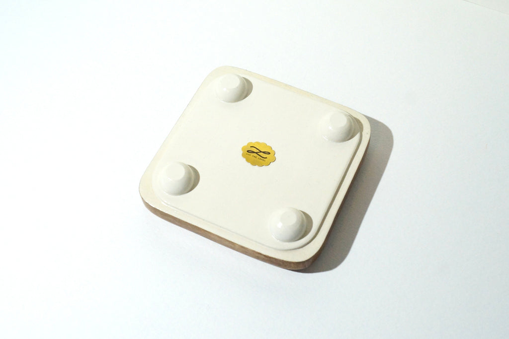 Bottom view of a handmade wooden jewelry tray featuring a cream-painted base, four rounded feet, and a gold Lou The Label brand emblem in the center.