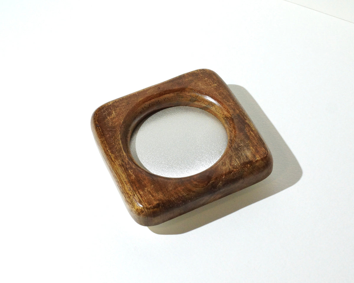 Small square wooden jewelry tray with rounded corners, a rich brown finish, visible wood grain, and a circular center lined with shimmering ivory satin fabric photographed on a white background.