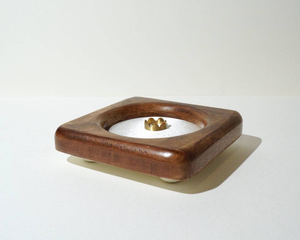 Side view of a handmade wooden jewelry tray with a rich brown finish, rounded square frame, ivory satin lining, and a gold ring resting in the center.